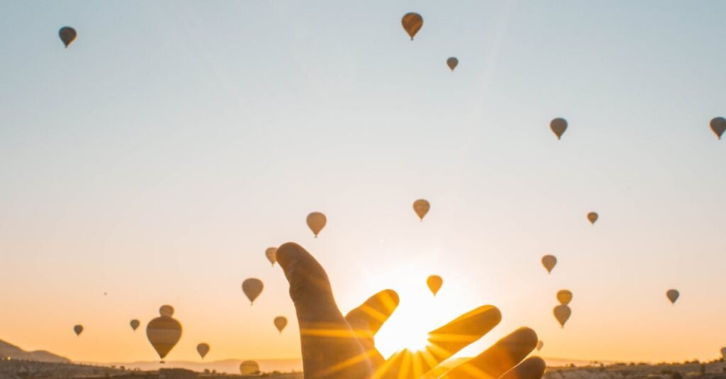 Experience the magic of hot air balloons at sunrise with an outstretched hand in Cappadocia's breathtaking landscape.