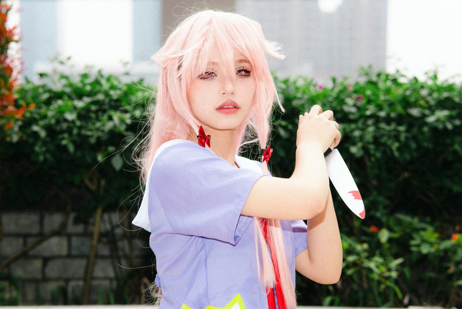 A woman in anime cosplay with pink hair and a knife, posing outdoors.