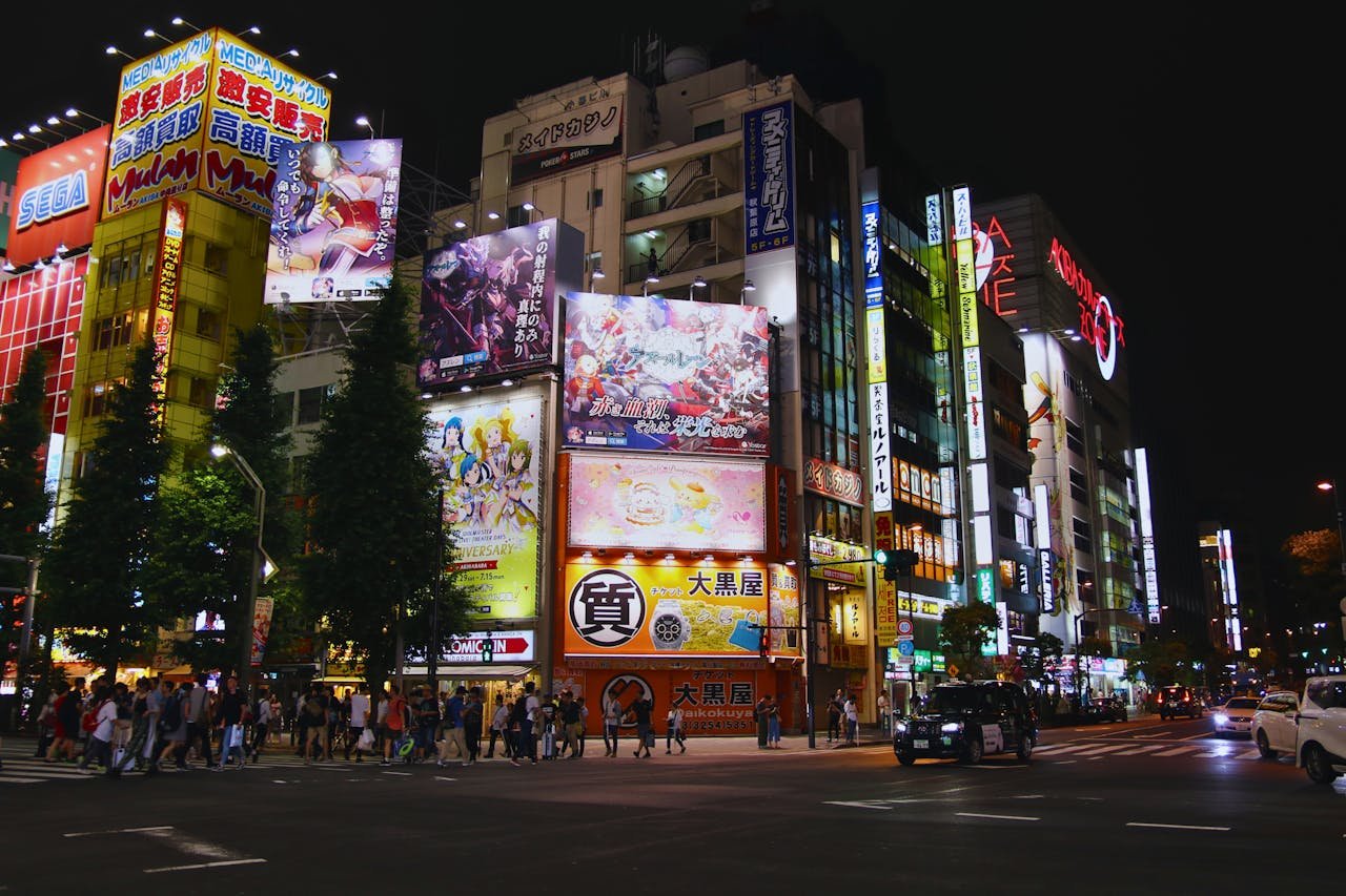 Bustling street scene in Akihabara, Tokyo at night with bright neon signs and animated billboards.